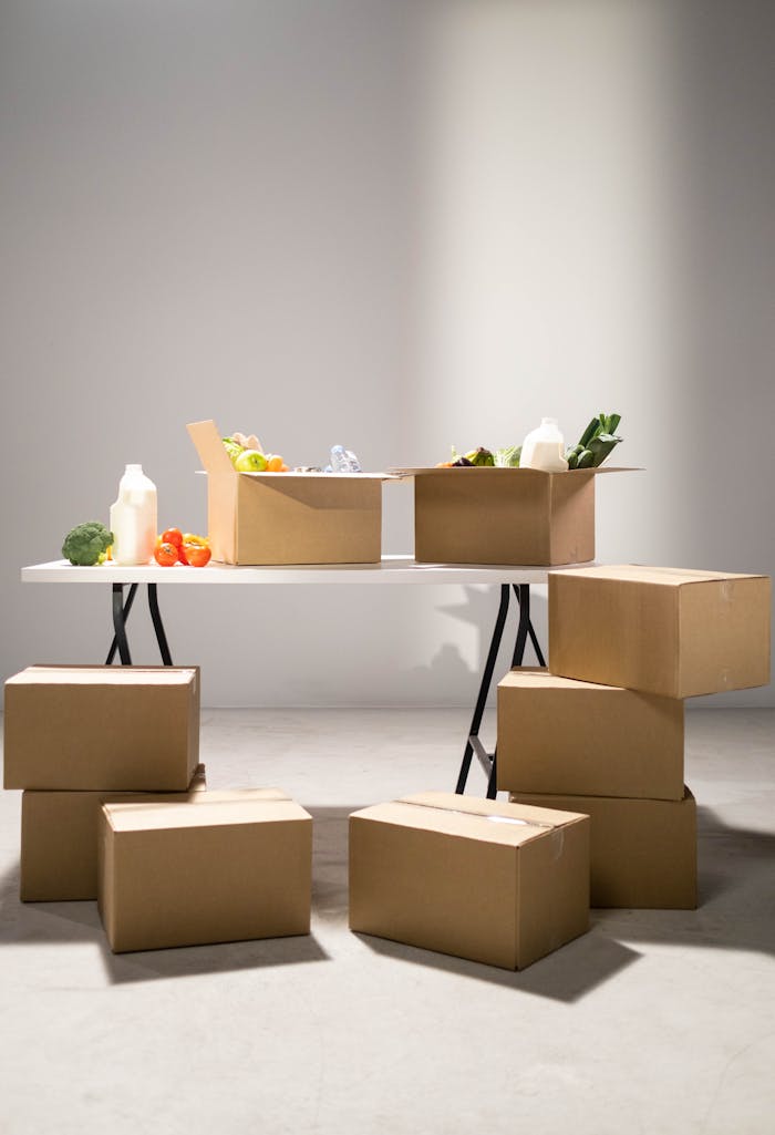 Avaleht Cardboard boxes filled with assorted groceries on a white folding table indoors.